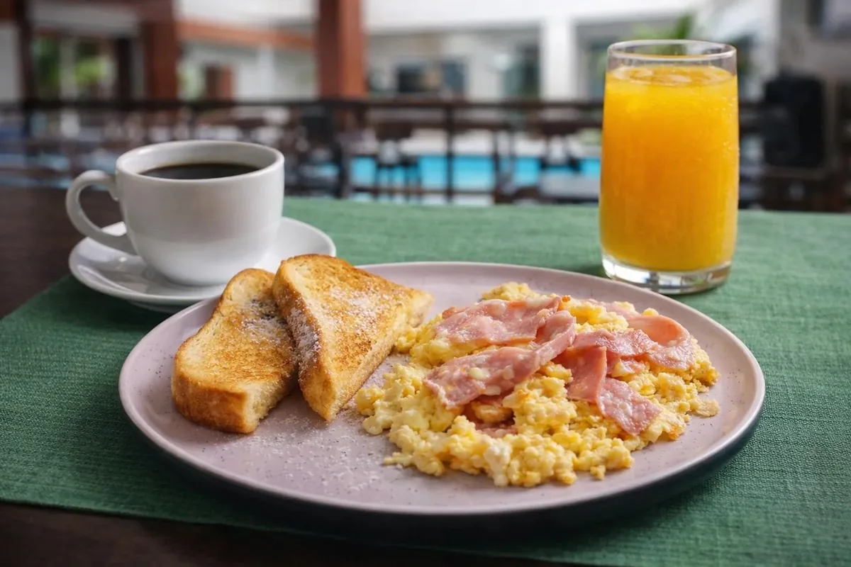 Desayuno americano con huevos revueltos, jamón, tostadas y jugo frente a la piscina